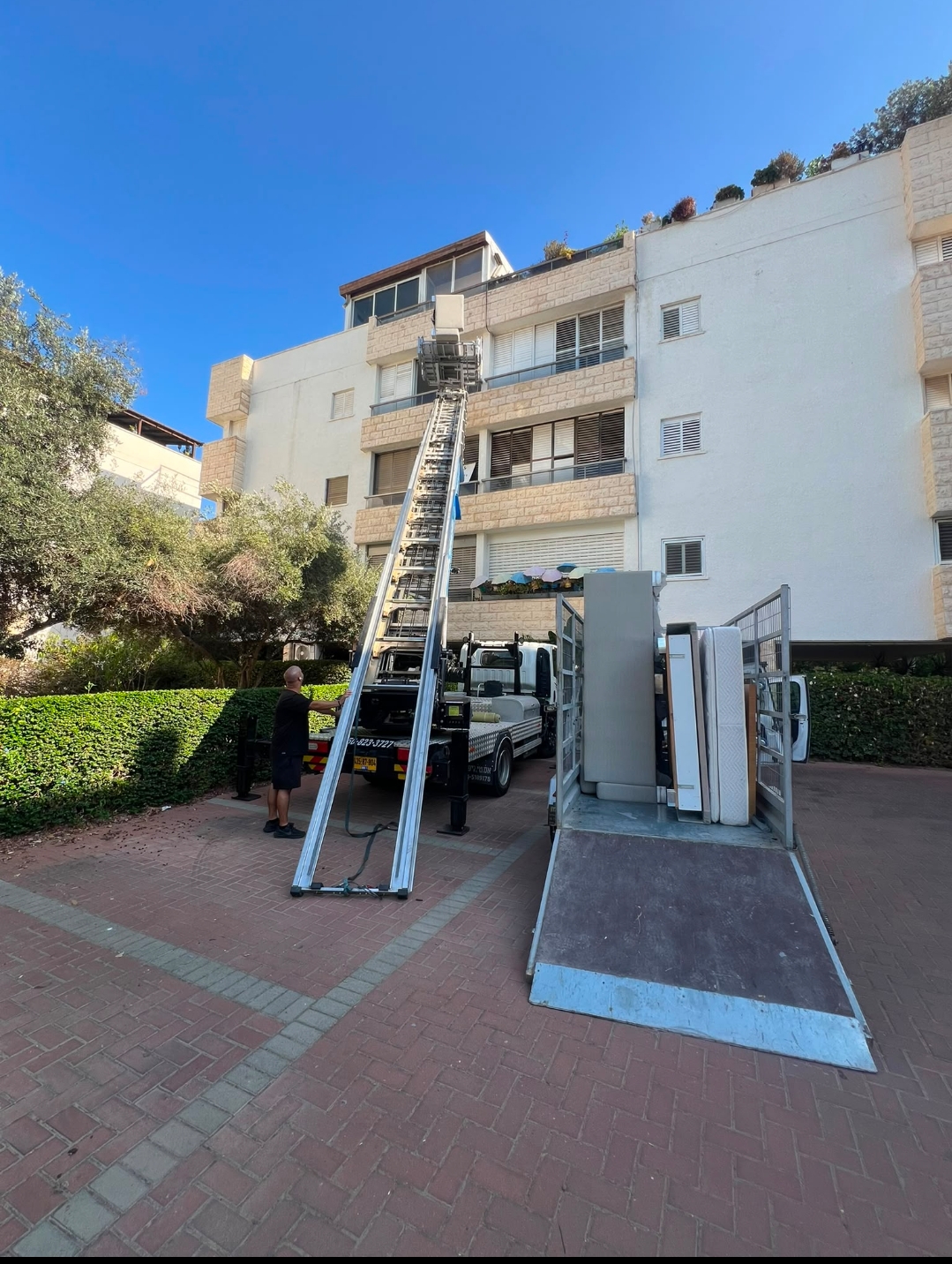 מנוף הובלות לצד נגרר עמוס מול בניין מגורים